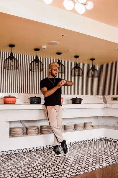 Dressed in a black round collar T-shirt and white pants man standing in the kitchen
